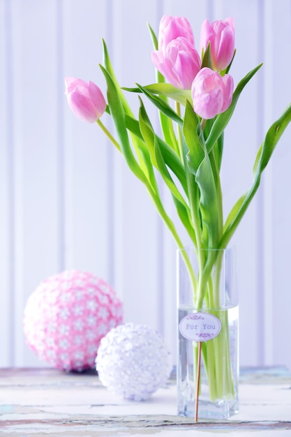 Mooie roze tulpen in vaas met decoratieve ballen op tafel op houten achtergrond