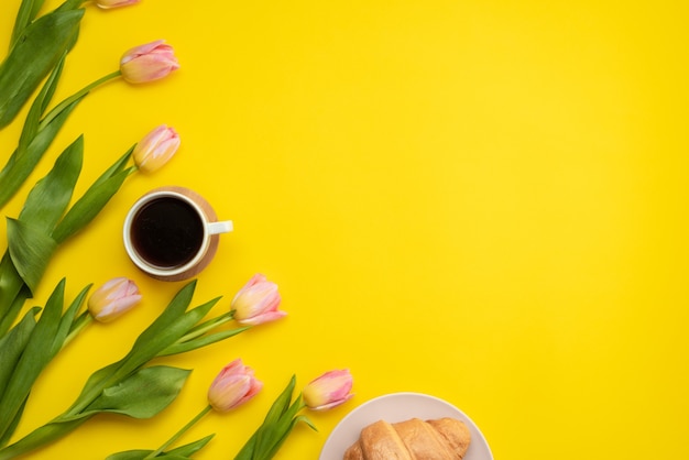 Mooie, roze tulpen, koffie en croissants op een gele achtergrond