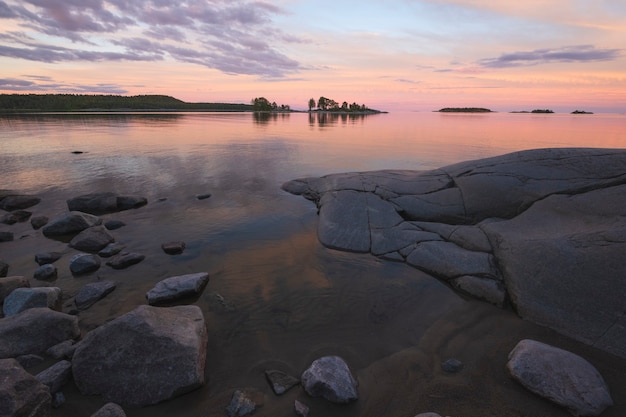 Mooie roze zonsondergang op het Ladogameer in Karelië, Rusland in het Nationale park van Ladoga Skerries in de zomer. Natuurlijk landschap met water rotsen, stenen eilanden en bos in de buurt van de kust