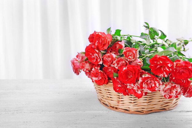 Mooie rozen in rieten mand op tafel op lichte achtergrond