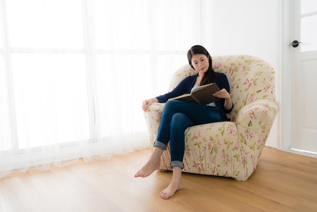 mooie rustige vrouw zittend op de bank bank ontspannen en stripboek lezen in de woonkamer op vakantie middag met raam achtergrond.