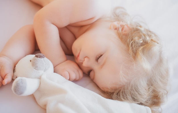 Mooie schattige baby die thuis in bed slaapt met speelgoedkind dat in bed slaapt