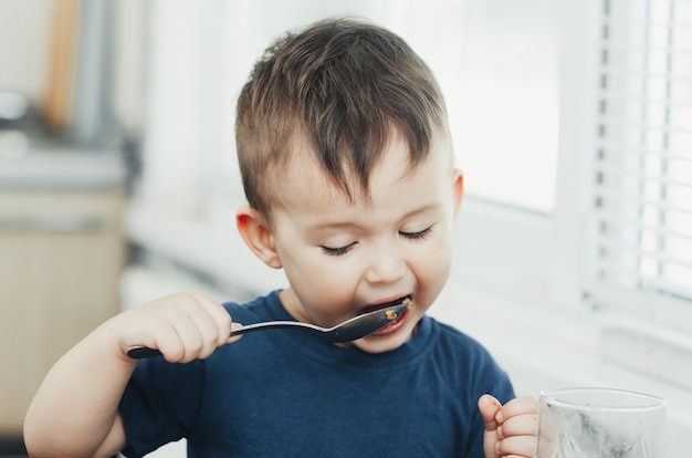 Mooie schattige baby eet rijst met een lepel in de keuken