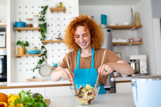 Mooie schattige jonge lachende vrouw in de keuken bereidt een veganistische salade in vrijetijdskleding