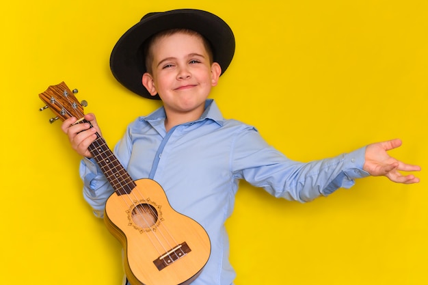 Mooie schattige kleine jongen in hoed en shirt houdt gitaar geïsoleerd op geel