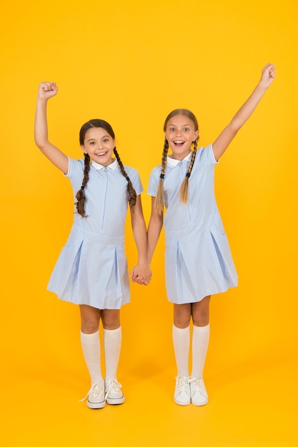 Mooie schoolmeisjes. Terug naar schoolconcept. Kapsalon. Leuke schoolmeisjes. Meisjes met gevlochten kapsel. Vrolijke schoolmeisjes gele achtergrond. Kleine meisjes spelen met schattige vlechten.