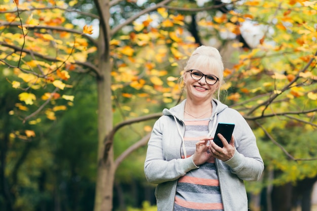 Mooie senior vrouw in een rugzak op een wandeling in het park, praten over de telefoon