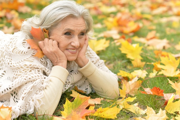 Mooie senior vrouw liggend op groen gras met kleurrijke herfstbladeren