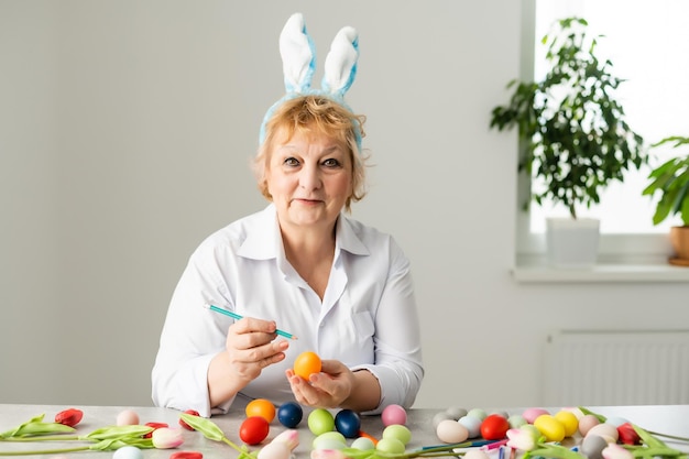 Mooie senior vrouw met paaseieren en paasbrood op tafel thuis.