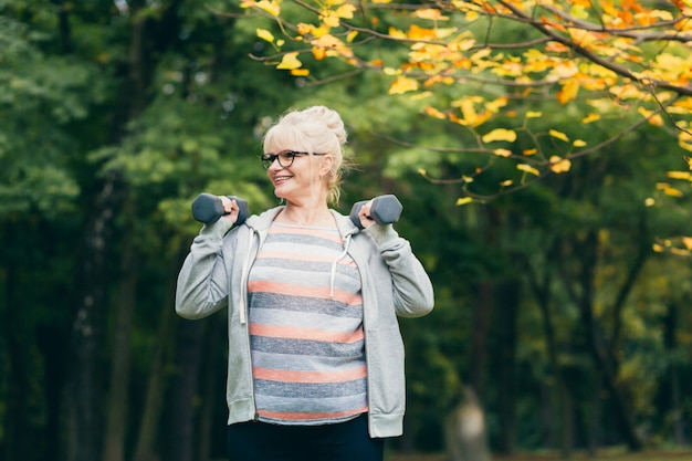 Mooie senior vrouw op een wandeling in het park, voert oefeningen met halters in haar handen