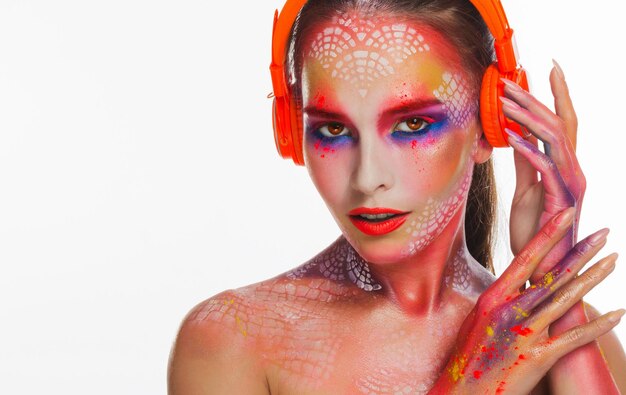 Mooie sensuele vrouw met heldere creatieve make-up die naar muziek luistert in oranje hoofdtelefoons, witte studioachtergrond, kopieerruimte