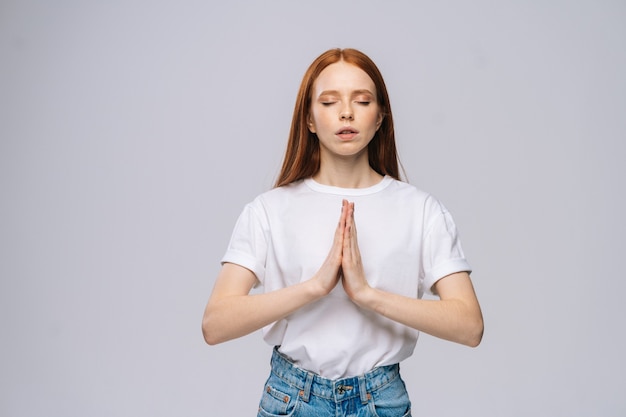 Mooie serene jonge vrouw die een t-shirt en een spijkerbroek draagt die de ogen gesloten houdt tijdens het mediteren