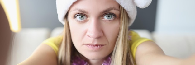 Foto mooie serieuze blonde jonge vrouw die zich voordeed op camera in santa claus hat