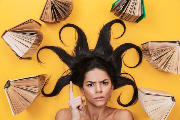 Foto mooie serieuze jonge vrouw ligt geïsoleerd op gele muur over boeken