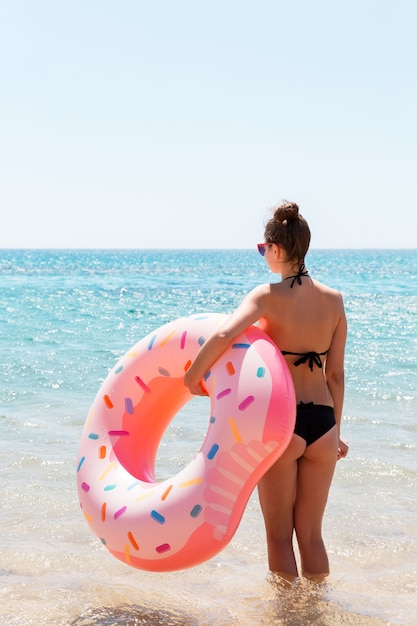 Mooie sexy schattige gelukkige vrouw die op het strand loopt met een roze rubberen opblaasbare ring in de hand. zomervakantie en vakantie concept.