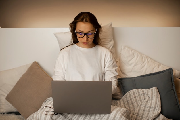 Mooie sexy zakenvrouw in glazen zit in bed met laptop