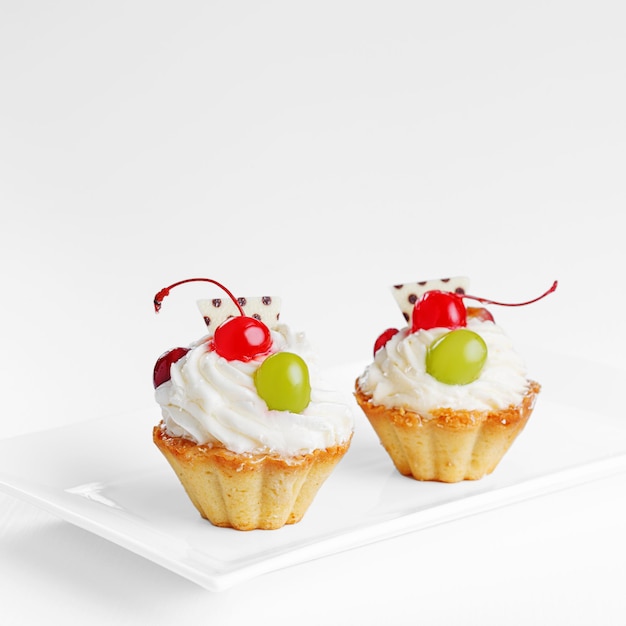 Mooie slagroomtaarten met kersen en druiven op een bord op een witte close-up als achtergrond