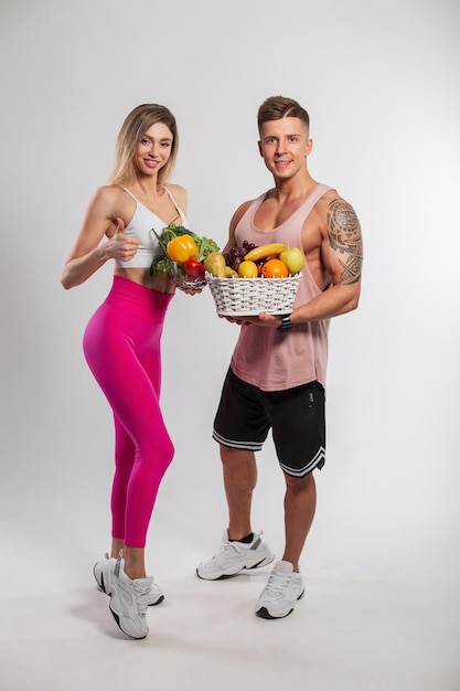 Mooie slanke fitness meisje en knappe atletische gespierde man met groenten en fruit op witte achtergrond in de studio Gezond veganistisch rauw voedsel