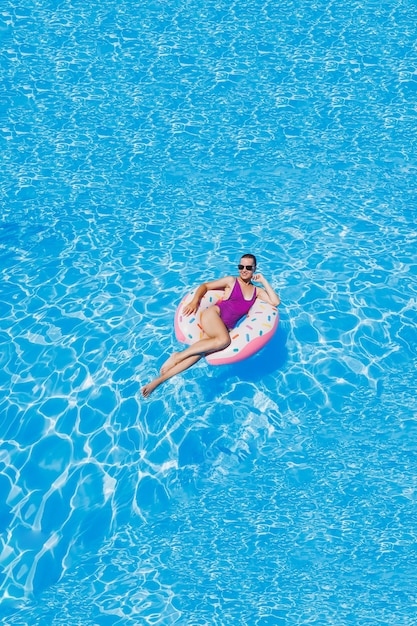 Mooie slanke jonge vrouw in een zwembroek genieten van het waterpark drijvend in een opblaasbare grote ring op een sprankelend blauw zwembad glimlachend in de camera zomervakantie