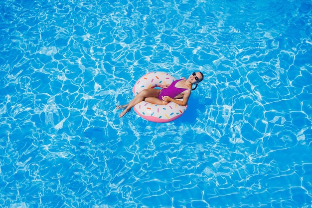 Mooie slanke jonge vrouw in een zwembroek genieten van het waterpark drijvend in een opblaasbare grote ring op een sprankelend blauw zwembad glimlachend in de camera zomervakantie