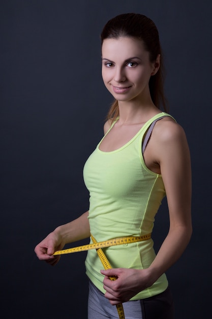 Mooie slanke sportieve vrouw met meetlint over grijze achtergrond