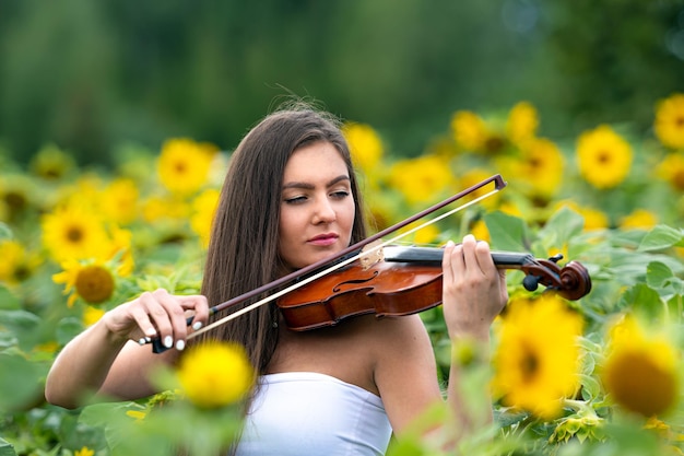 Mooie slanke tienervrouw met viool in geel bloeiend zonnebloemgebied