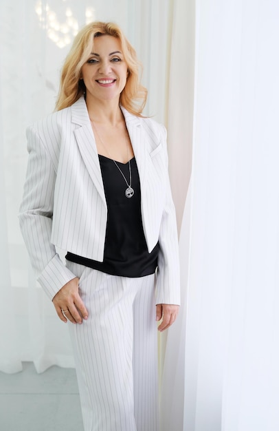Mooie slanke volwassen vrouw ondernemer in witte broek en jas kijkt naar de camera en glimlacht Concept van kleine bedrijven en vrouwelijke ondernemers