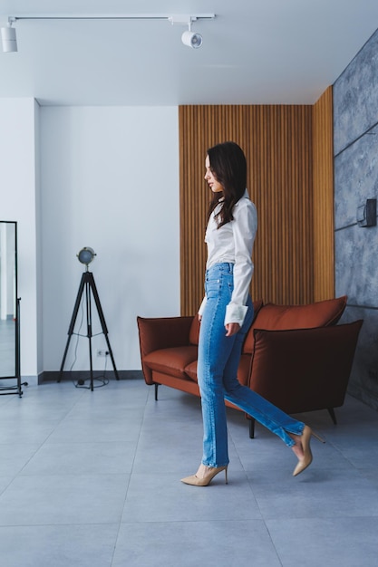 Mooie slanke vrouw in klassieke beige schoenen met dunne hakken en jeans en een wit overhemd Stijlvol meisje op hoge hakken loopt vol vertrouwen