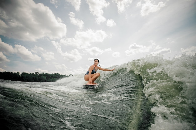 Mooie slanke vrouw wakesurfing op het bord tegen de hemel