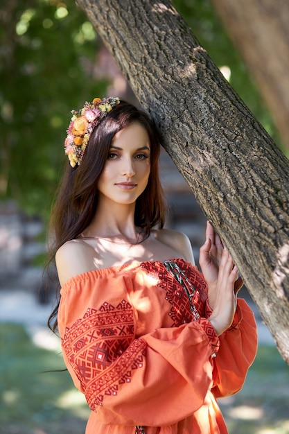 Mooie Slavische vrouw in een oranje etnische jurk en een krans van bloemen op haar hoofd. Mooie natuurlijke make-up