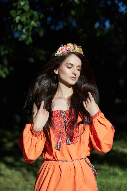 Mooie Slavische vrouw in een oranje etnische jurk en een krans van bloemen op haar hoofd