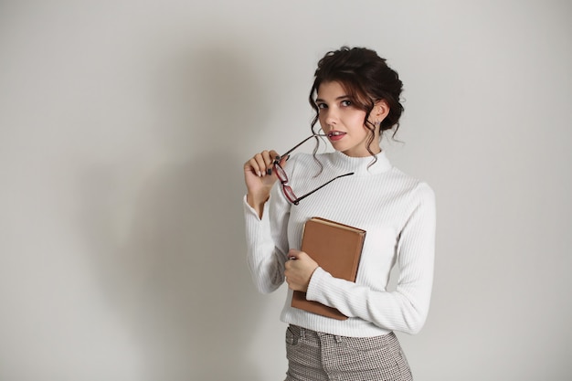 Mooie slimme jonge vrouw met een boek in haar handen en glazen.