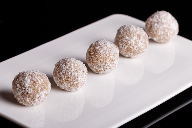 Mooie snoepjes met kokos op een witte plaat op een zwarte achtergrond