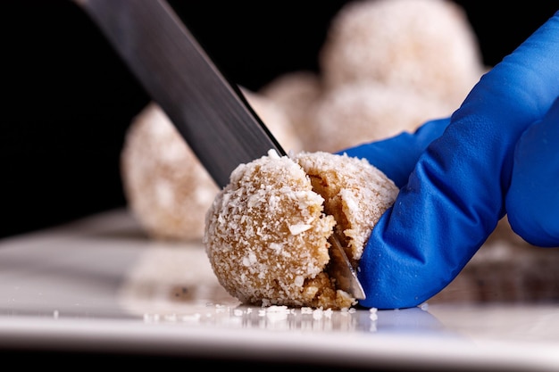 Mooie snoepjes met kokos worden gesneden met een mes op een witte plaat op een zwarte achtergrond