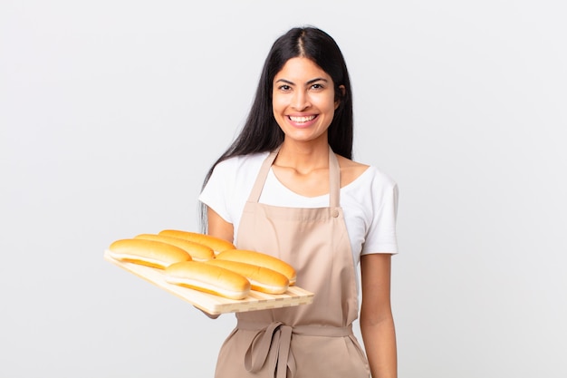 mooie Spaanse chef-kokvrouw die gelukkig glimlacht met een hand op de heup en zelfverzekerd en een dienblad met broodbroodjes vasthoudt