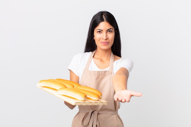 Mooie Spaanse chef-kokvrouw die vrolijk lacht met vriendelijk en een concept aanbiedt en toont en een dienblad met broodbroodjes vasthoudt