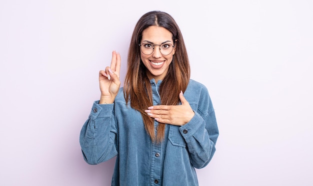 Mooie Spaanse vrouw die er gelukkig, zelfverzekerd en betrouwbaar uitziet, glimlacht en een overwinningsteken toont, met een positieve houding