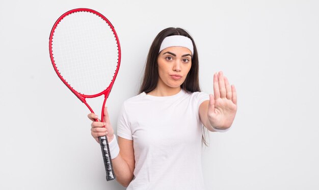 Mooie Spaanse vrouw die er serieus uitziet en open palm toont die een tennisconcept met een stopgebaar maakt