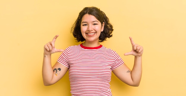 Mooie Spaanse vrouw die haar eigen glimlach inkadert of schetst met beide handen en er positief en gelukkig wellnessconcept uitziet