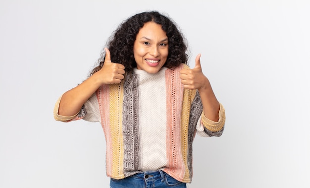 Mooie Spaanse vrouw die lacht en er in het algemeen gelukkig, positief, zelfverzekerd en succesvol uitziet, met beide duimen omhoog