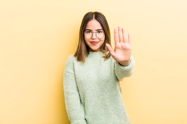 Mooie spaanse vrouw die lacht en er vriendelijk uitziet met nummer vijf of vijfde met hand vooruit aftellend