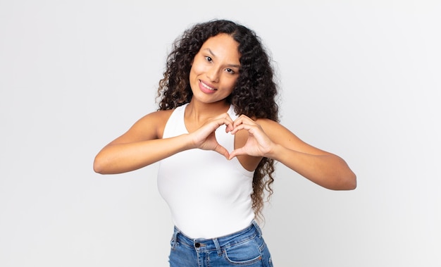 Mooie Spaanse vrouw die lacht en zich gelukkig voelt, schattig romantisch en verliefd maakt hartvorm met beide handen