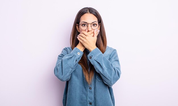 Mooie Spaanse vrouw die mond bedekt met handen met een geschokte verbaasde uitdrukking die een geheim houdt of oeps zegt