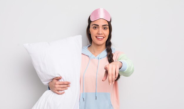 Mooie Spaanse vrouw die naar de camera wijst en je pyjama's en kussenconcept kiest