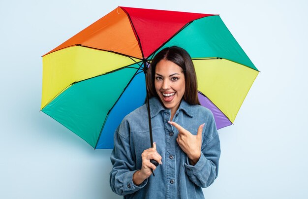 Mooie Spaanse vrouw die opgewonden en verrast kijkt en naar de zijkant wijst. paraplu concept