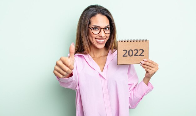 Mooie Spaanse vrouw die trots is, positief glimlacht met duimen omhoog. 2022 kalenderconcept