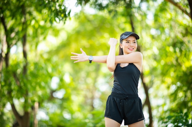 Mooie Sport Aziatische vrouw van middelbare leeftijd die haar armen strekt en wegkijkt voor een fitnesstraining in het park