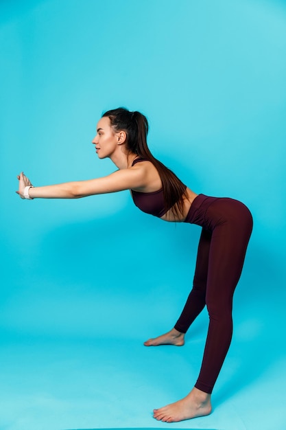 Mooie sportieve brunette vrouw die sportoefeningen doet buigt naar voren op een blauwe achtergrond. geïsoleerd.