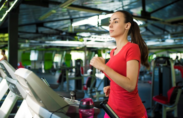 Mooie sportieve slanke jonge vrouw in fitness slijtage is joggen op de loopband in de sportschool.