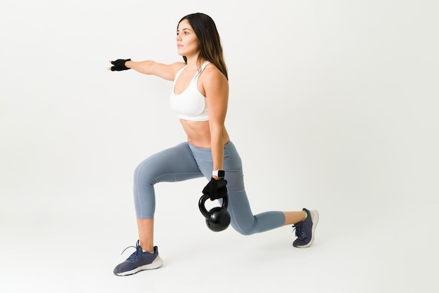 Mooie sportieve vrouw die lunges doet terwijl ze een kettlebell vasthoudt. Fit sterke atleet die traint met gewichten voor haar dagelijkse trainingsprogramma